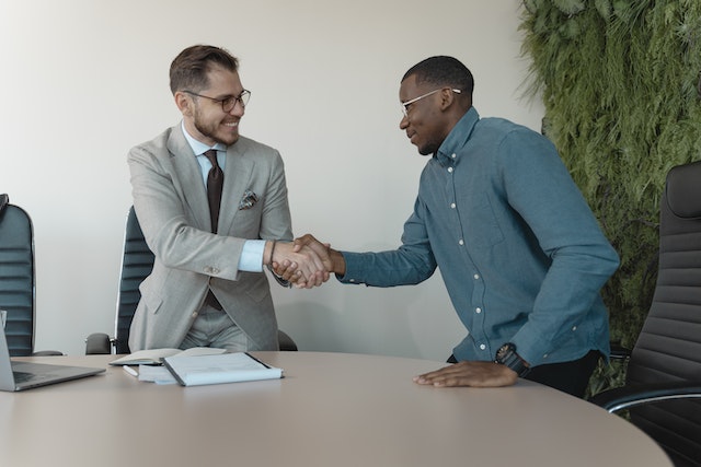 two people standing at a table and shaking hands